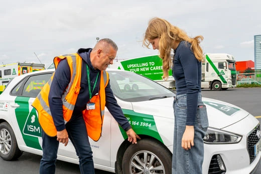 A_driving_instructor_and_young_woman_standing_next_to_a_car_ISM_Driving_lessons