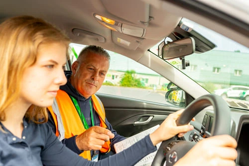 A_driving_instructor_and_young_woman_seated_in_a_car_ISM_Driving_lessons