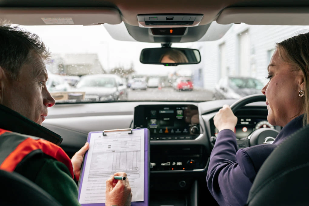 Driving_instructor_and_woman_are_seated_in_a_car_talking_and_examining_ISM_Driving_Lessons