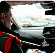 A_man_wearing_an_orange_vest_sits_in_the_driver's_seat_of_a_car_ISM_Driving_lessons
